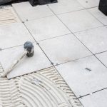 Układanie płytek ceramicznych na kleju rozprowadzonym pacą zębatą podczas prac wykończeniowych