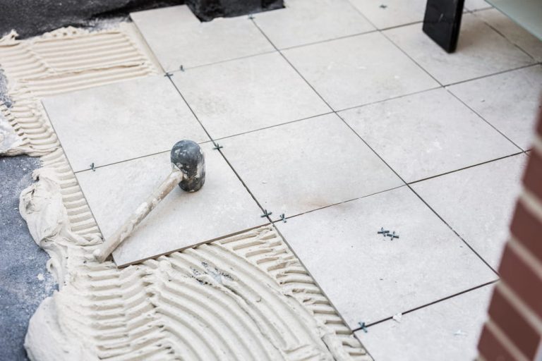 Układanie płytek ceramicznych na kleju rozprowadzonym pacą zębatą podczas prac wykończeniowych